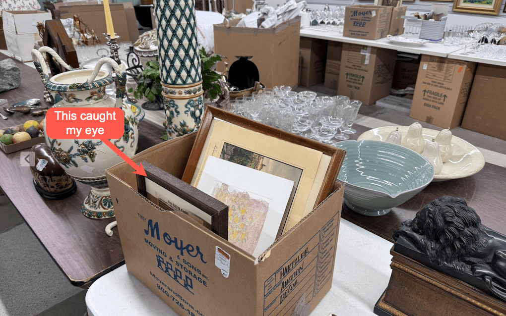 Objects to be sold in an auction house include a box filled with framed prints.